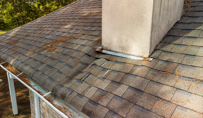 A house roof with damaged and missing shingles near a chimney